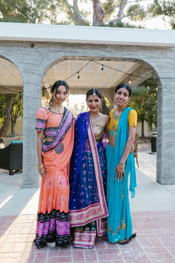 Three women wearing colorful traditional sarees enjoying an outdoor celebration.